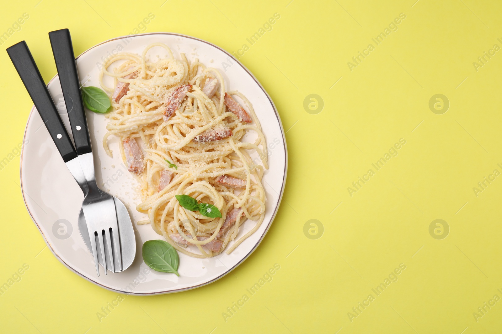 Photo of Plate of tasty pasta Carbonara with basil leaves on yellow background, top view. Space for text