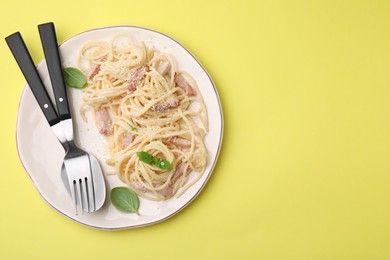 Photo of Plate of tasty pasta Carbonara with basil leaves on yellow background, top view. Space for text