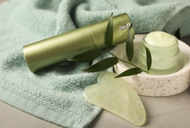 Photo of Jade gua sha tool, skin care products and towel on grey table