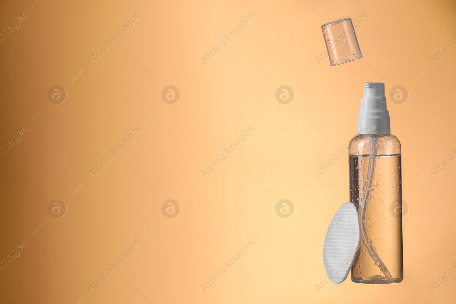 Photo of Wet bottle with micellar water and cotton pad on pale orange background. Space for text