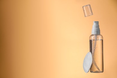 Photo of Wet bottle with micellar water and cotton pad on pale orange background. Space for text