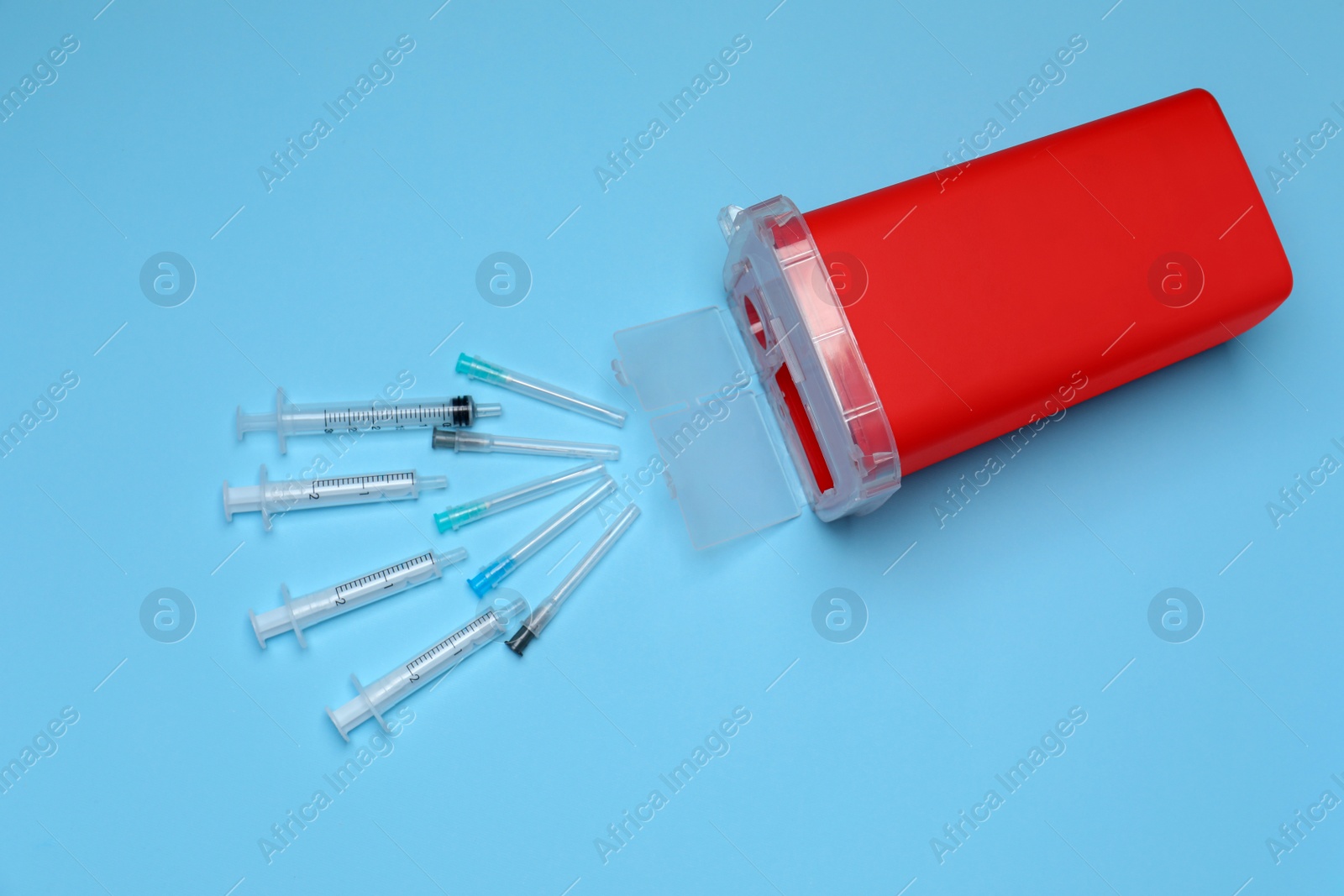 Photo of Disposable syringes, needles and sharps container on light blue background