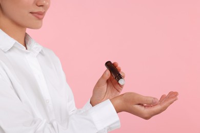 Woman with roller bottle applying essential oil onto wrist on pink background, closeup