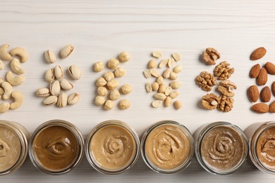 Many tasty nut butters in jars and nuts on white wooden table, flat lay