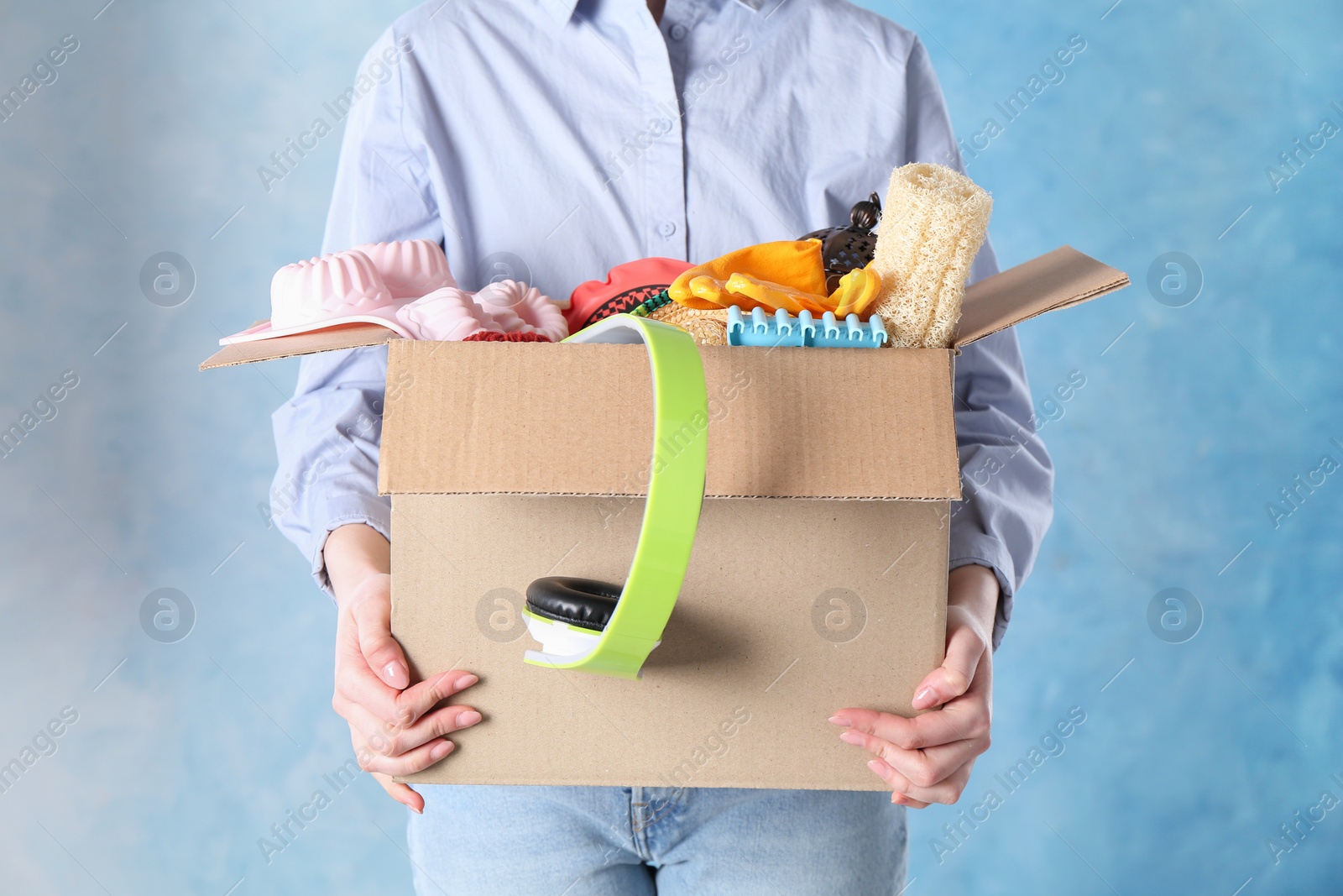 Photo of Woman holding box of unwanted stuff on blue background, closeup