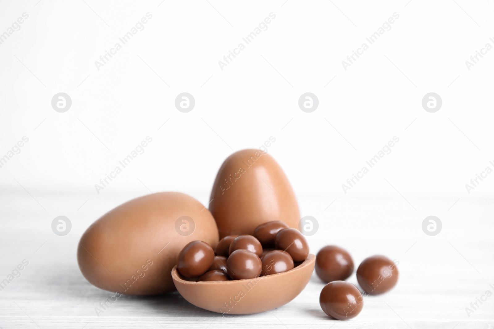 Photo of Whole and broken chocolate eggs with candies on white wooden table