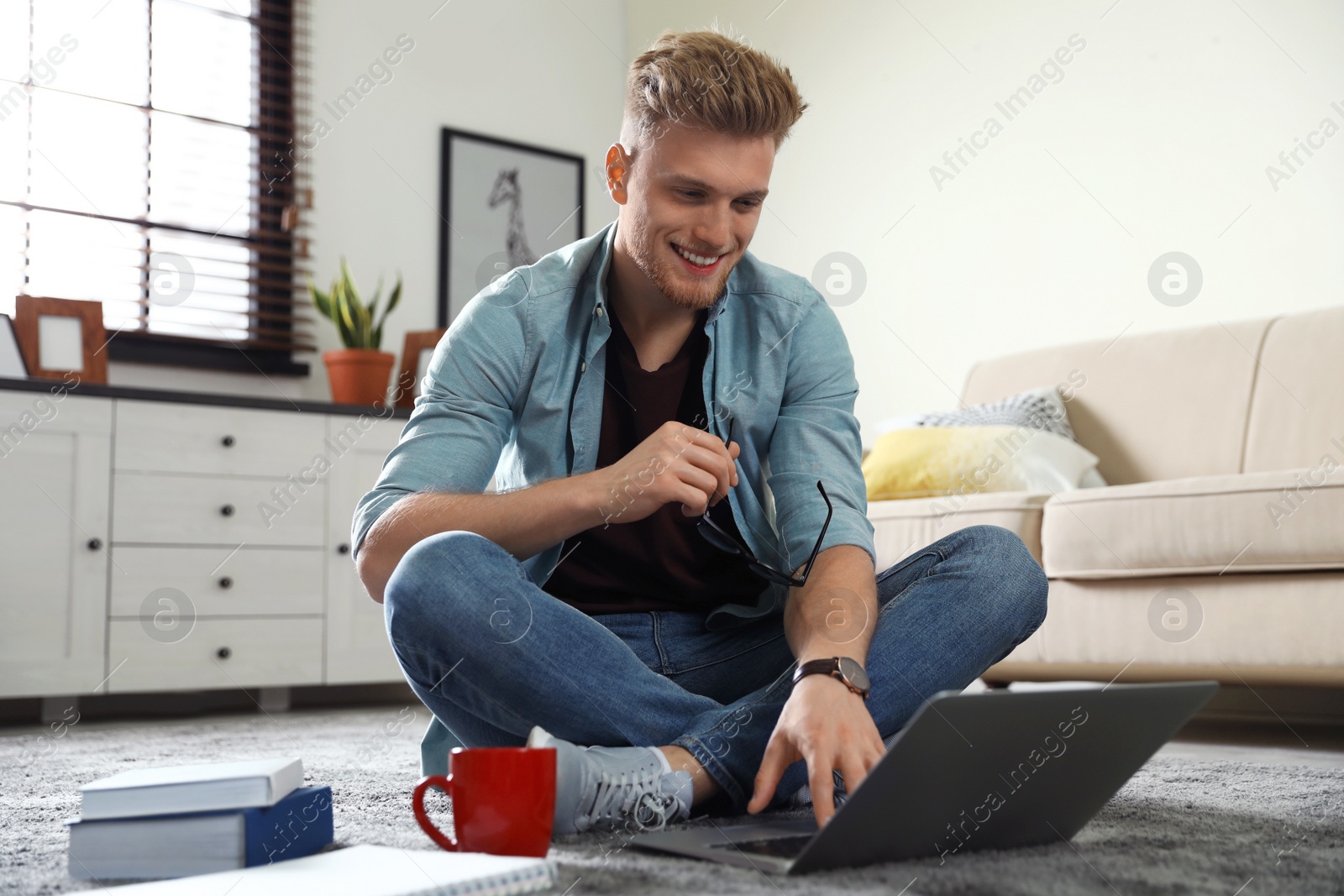 Photo of Young man using laptop while sitting on floor in living room