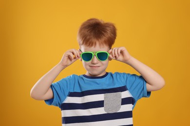 Cute little boy with sunglasses on yellow background