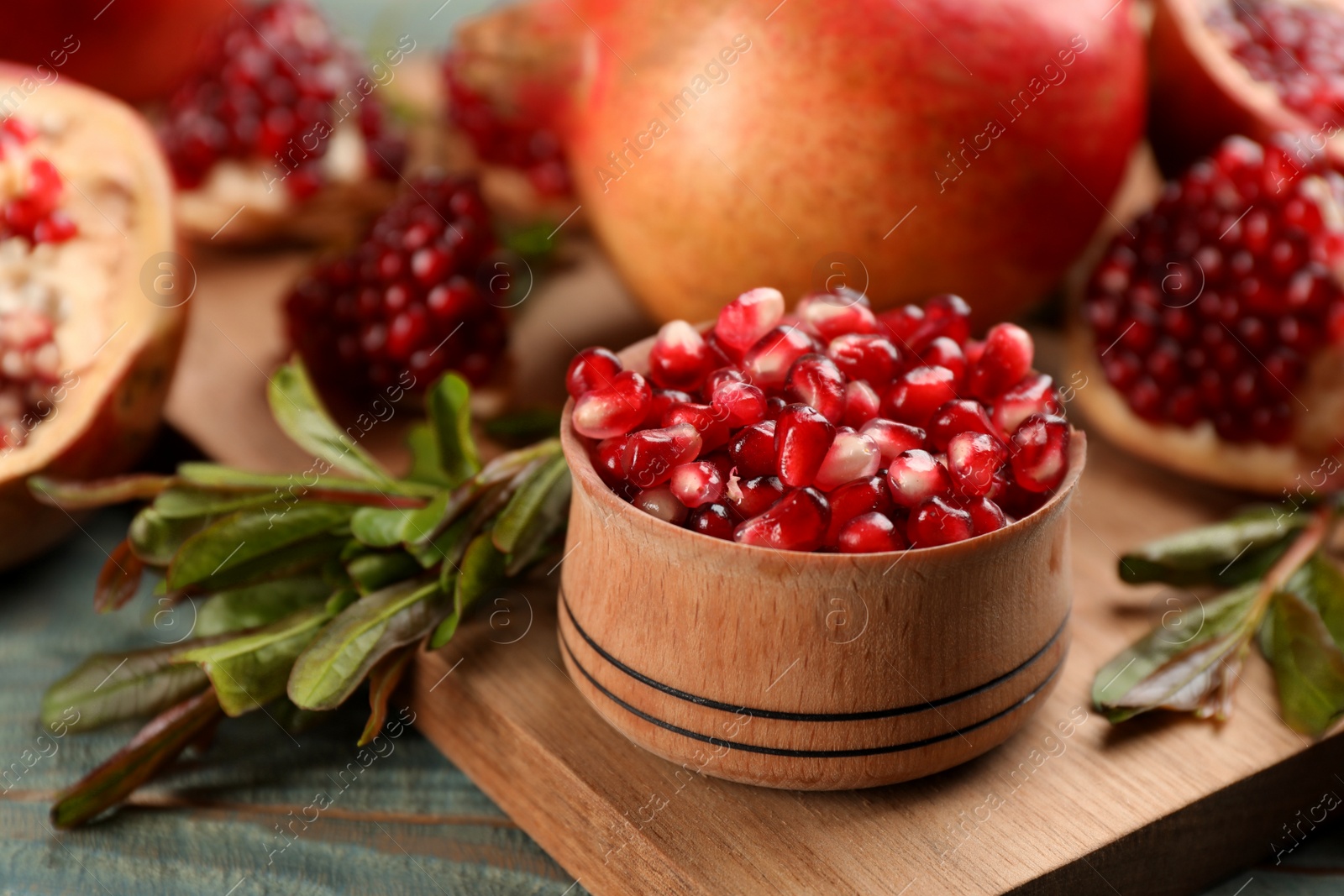 Photo of Delicious ripe pomegranate kernels in bowl on wooden board, closeup