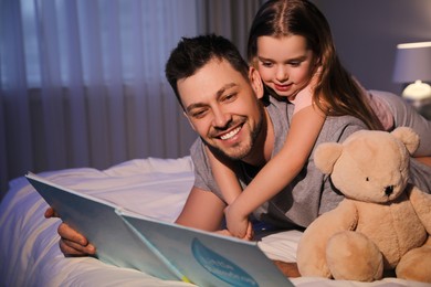 Photo of Father with his daughter reading book in bed at home