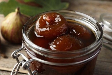 Jar of tasty sweet jam and fresh figs on wooden table, closeup