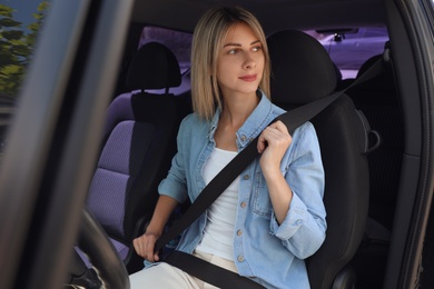 Woman fastening safety belt on driver's seat in car