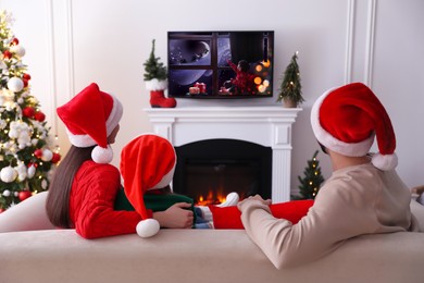 Image of Family watching festive movie on TV in room decorated for Christmas, back view
