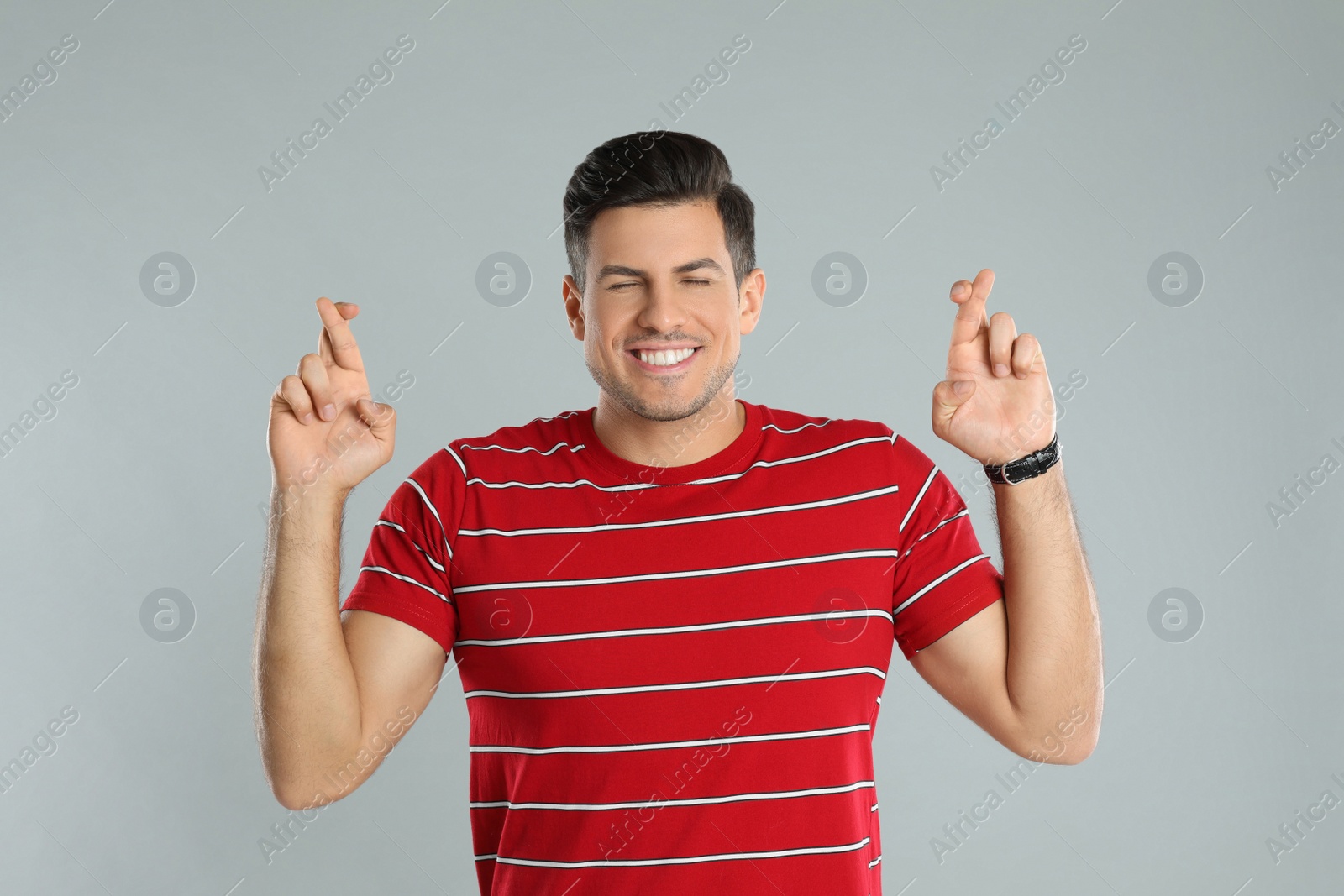 Photo of Man with crossed fingers on grey background. Superstition concept