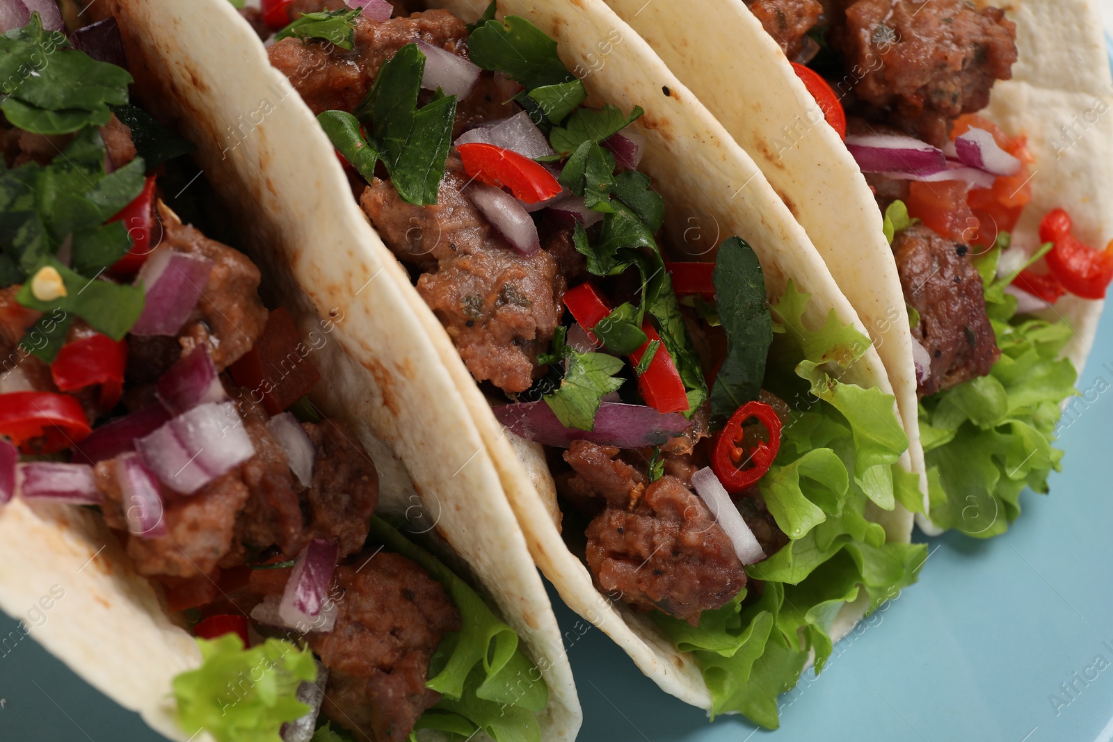 Photo of Delicious tacos with meat and vegetables on light blue table, closeup