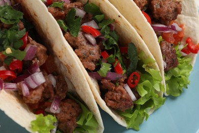 Photo of Delicious tacos with meat and vegetables on light blue table, closeup