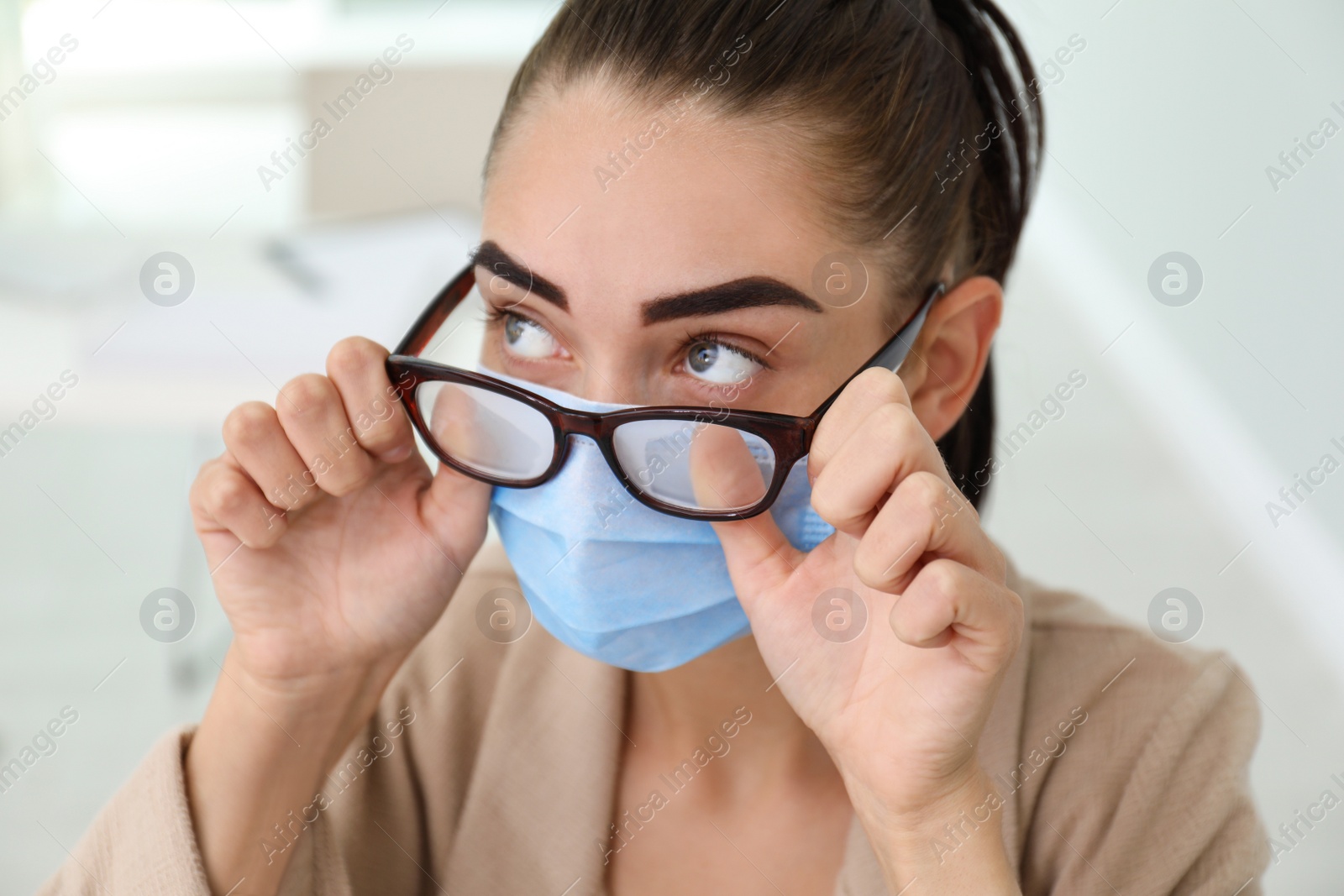 Photo of Woman wiping foggy glasses caused by wearing medical mask indoors, closeup