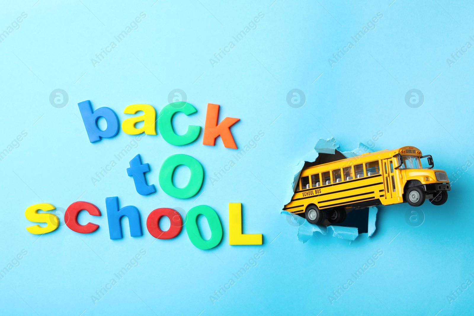 Photo of Yellow school bus and phrase "Back to school" on light blue background, flat lay. Transport for students