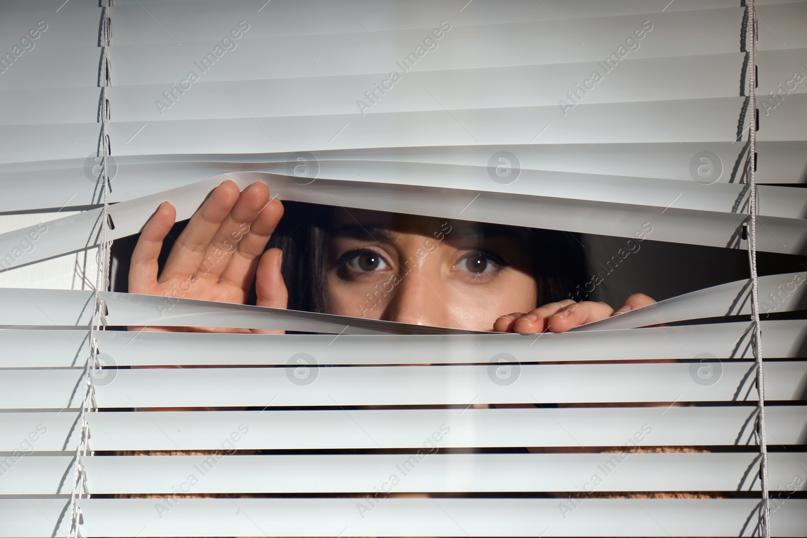 Photo of Curious woman looking through Venetian window blinds