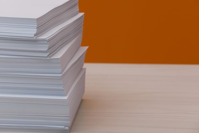 Photo of Stack of paper sheets on white wooden table near orange wall. Space for text