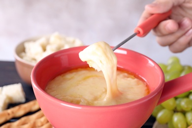 Photo of Woman dipping bread piece into pot with cheese fondue, closeup