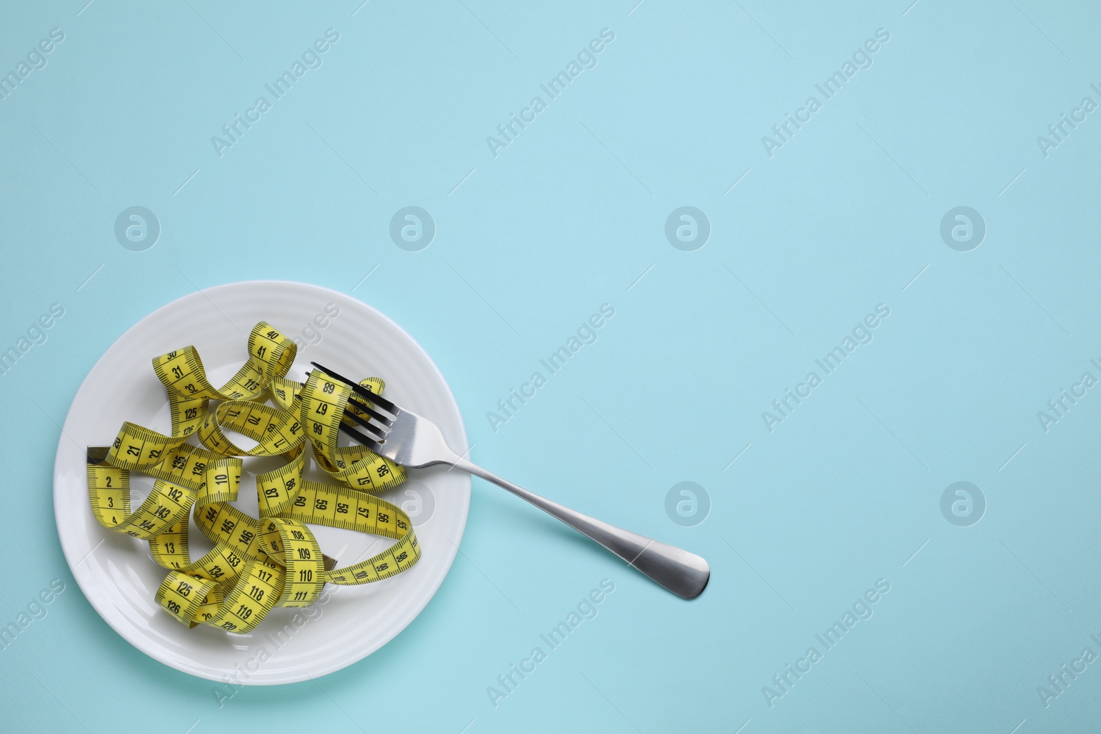 Photo of Measuring tape and fork on light blue background, top view with space for text. Weight loss concept