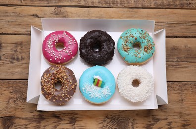 Box with different tasty glazed donuts on wooden table, top view