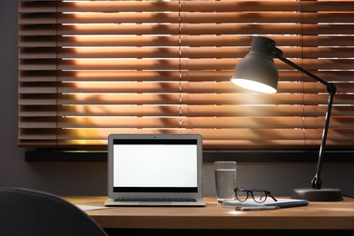 Photo of Modern laptop and lamp on table near window in office