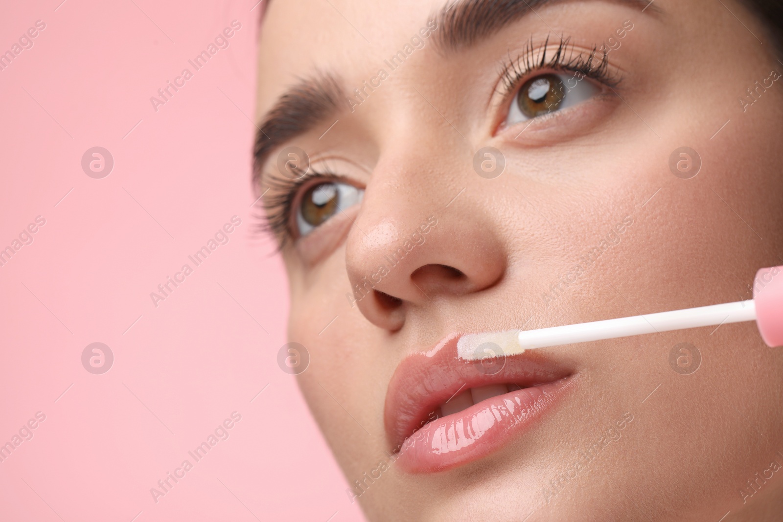 Photo of Woman applying lip gloss on pink background, space for text