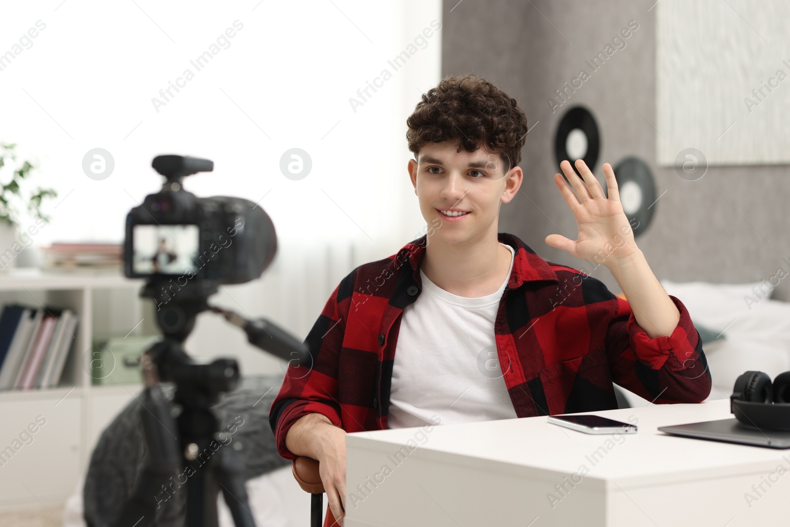 Photo of Smiling teenage blogger waving hello to his subscribers while streaming at home