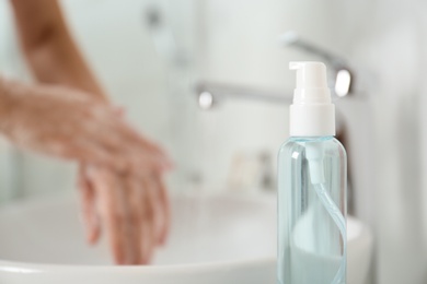 Photo of Bottle of antibacterial soap and blurred woman washing hands on background. Personal hygiene during COVID-19 pandemic