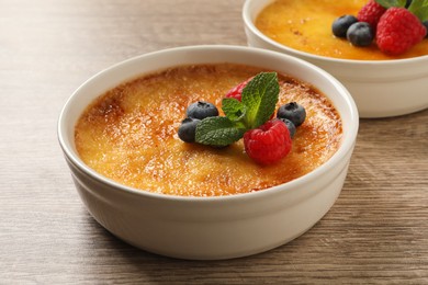 Photo of Delicious creme brulee with fresh berries on wooden table