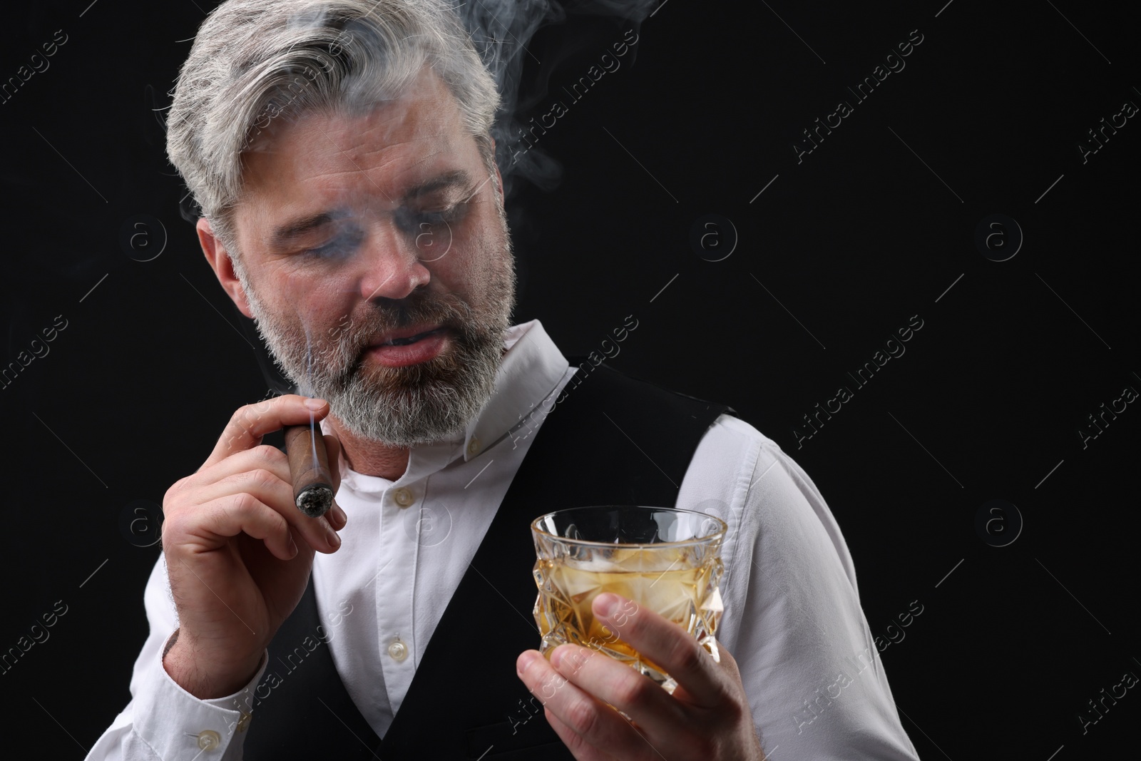 Photo of Bearded man with glass of whiskey smoking cigar against black background. Space for text