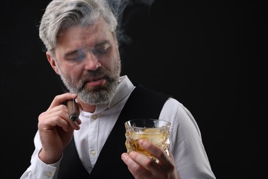 Bearded man with glass of whiskey smoking cigar against black background. Space for text