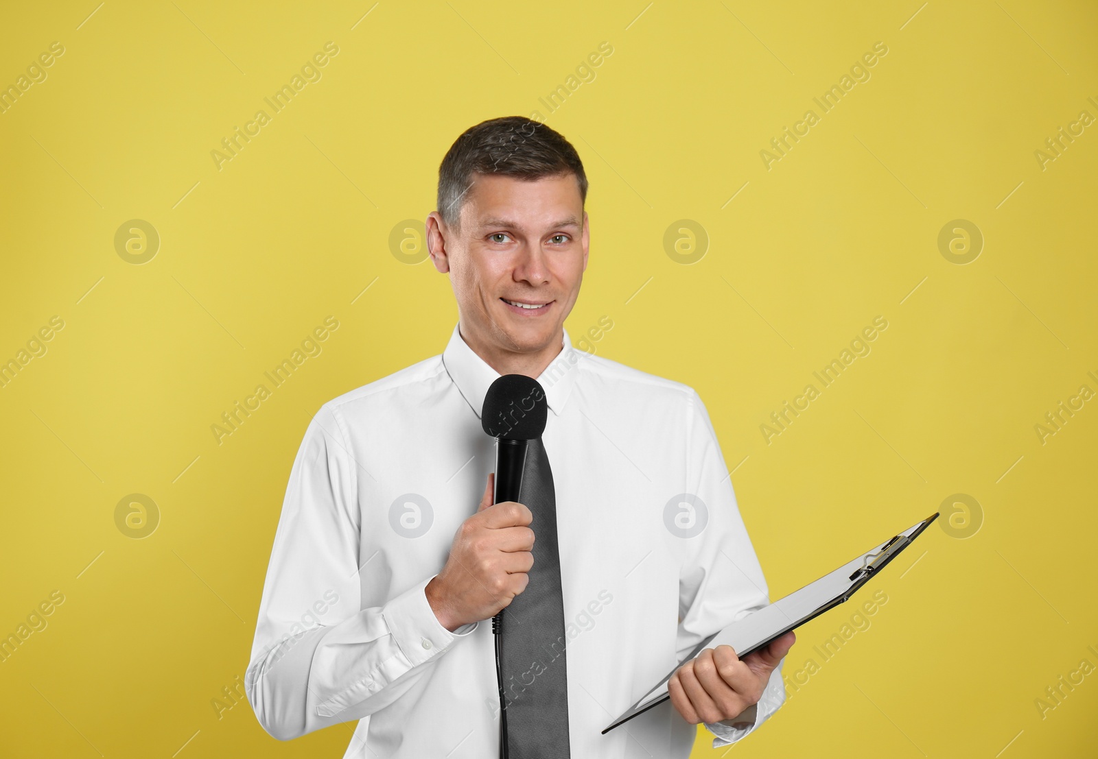 Photo of Male journalist with microphone and clipboard on yellow background