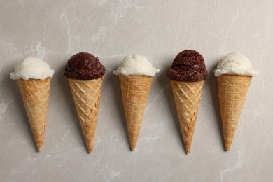 Photo of Tasty ice cream scoops in waffle cones on light marble table, flat lay