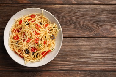 Photo of Bowl of delicious pasta with olives, tomatoes and parmesan cheese on wooden table, top view. Space for text