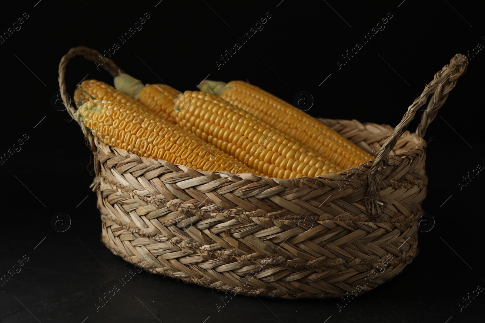 Photo of Corn cobs in basket on black table