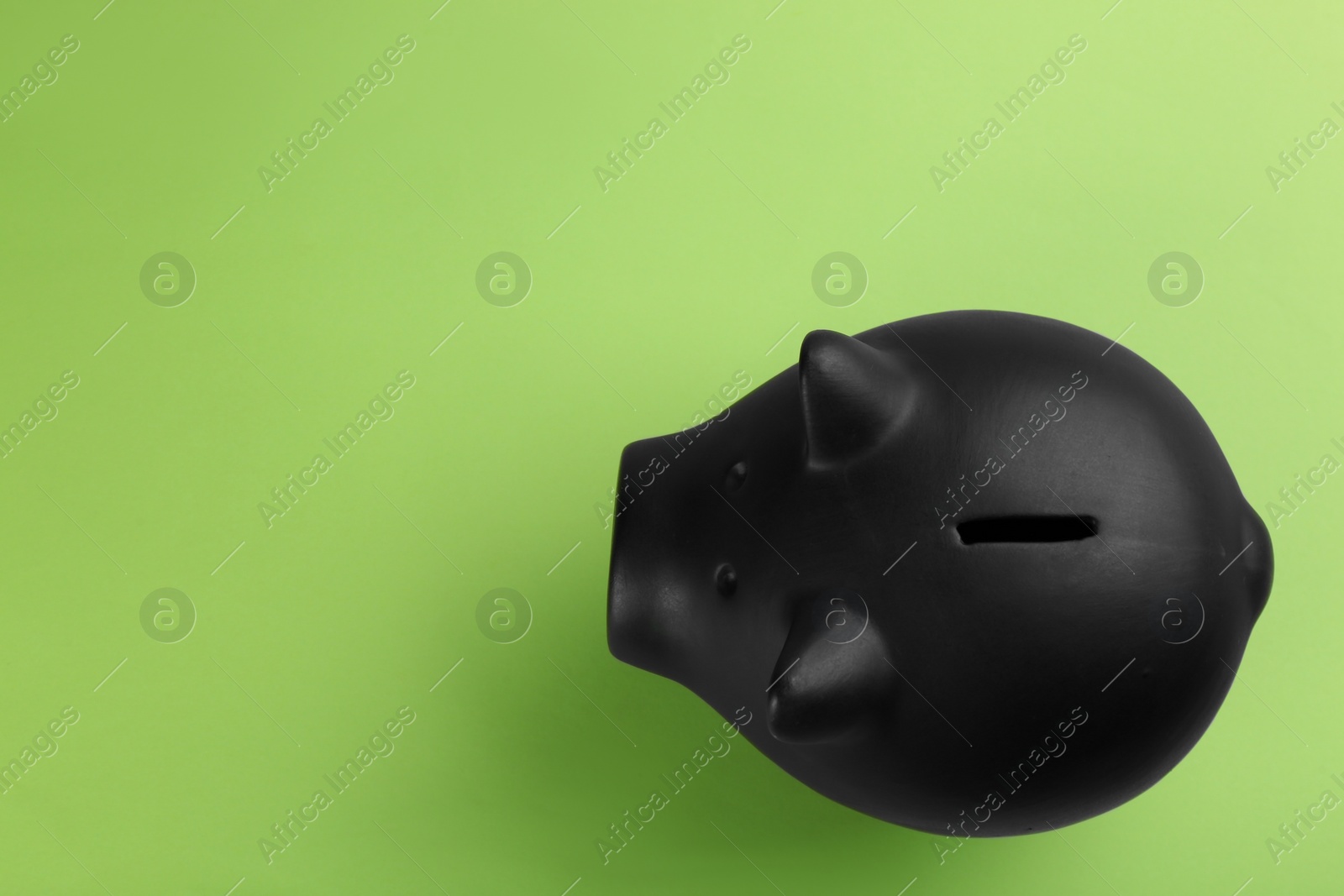 Photo of Black piggy bank on green background, top view. Space for text
