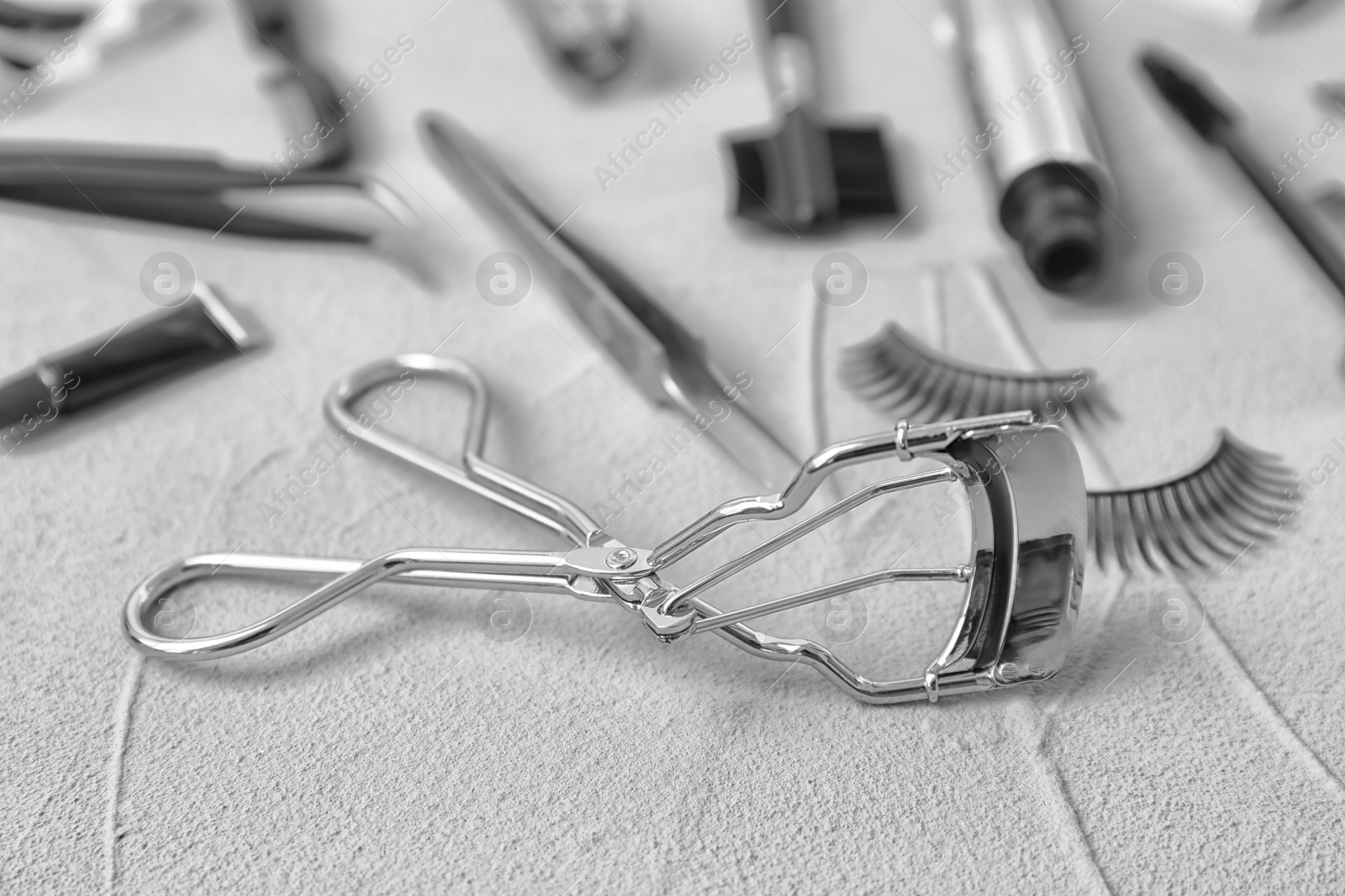 Photo of Eyelash curler and cosmetic tools on grey background, closeup