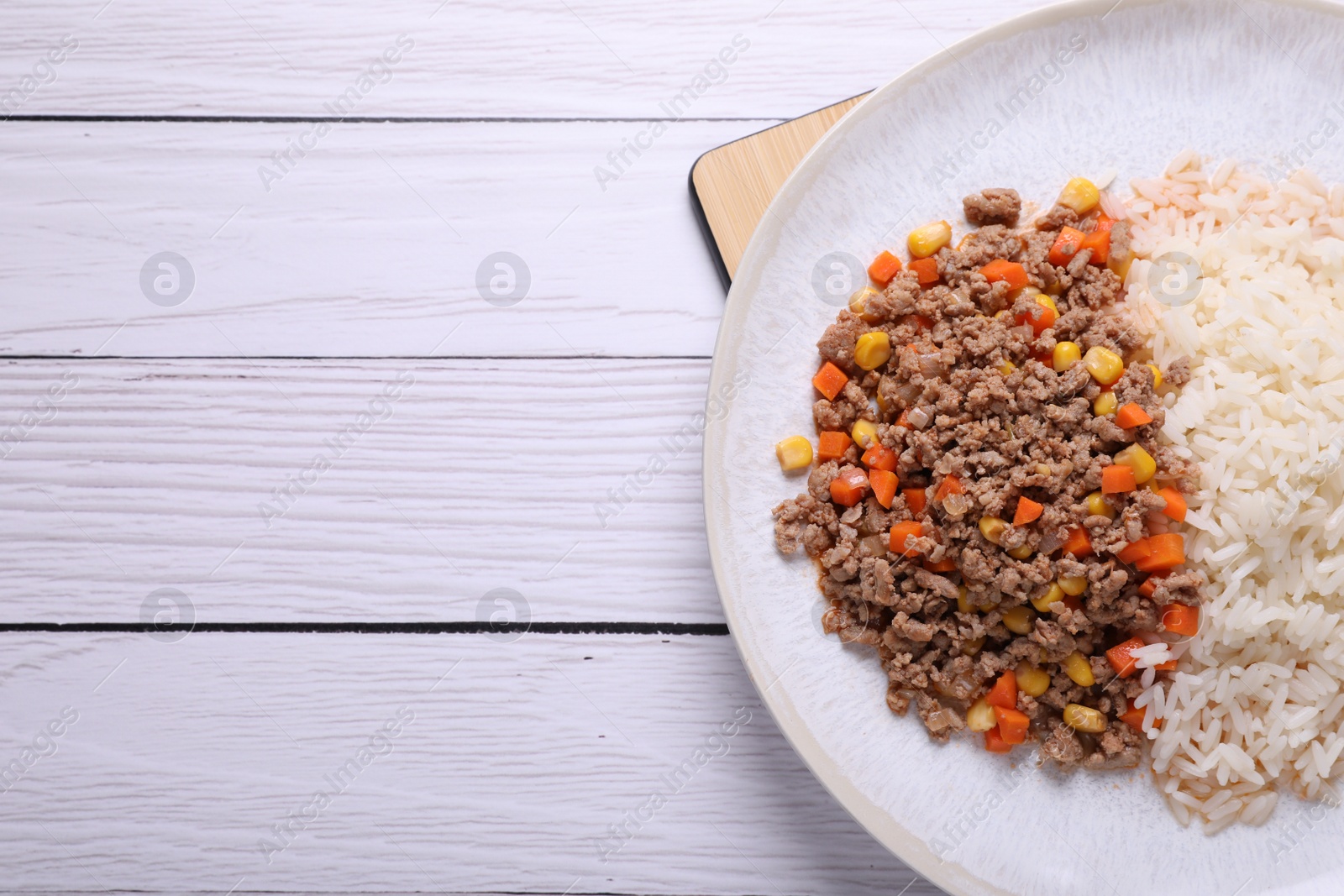 Photo of Tasty dish with fried minced meat, rice, carrot and corn on white wooden table, top view. Space for text