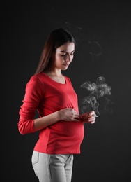 Pregnant woman smoking cigarette on black background