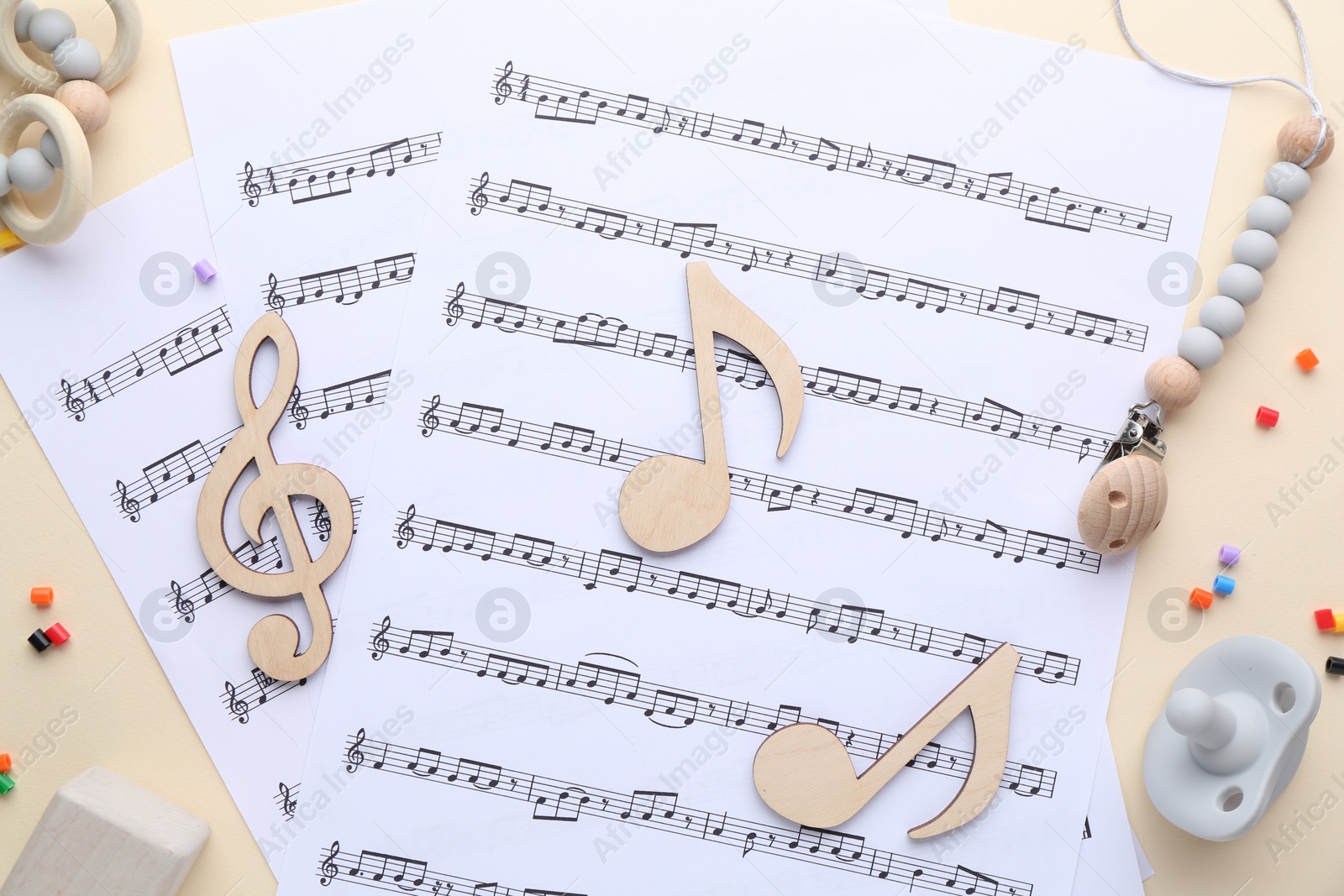 Photo of Wooden notes, music sheets and toys on beige background, flat lay. Baby song concept
