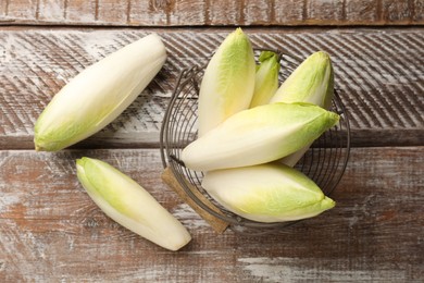 Photo of Fresh raw Belgian endives (chicory) in metal basket on wooden table, top view