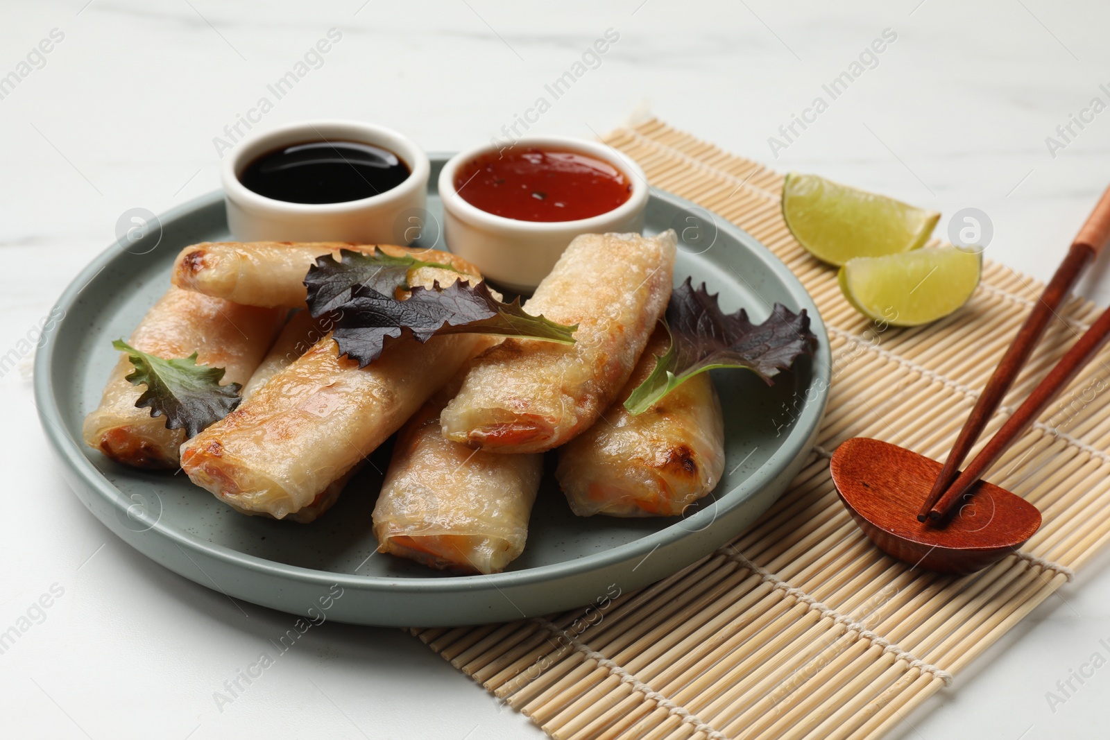 Photo of Tasty fried spring rolls, lettuce, lime and sauces on white marble table, closeup