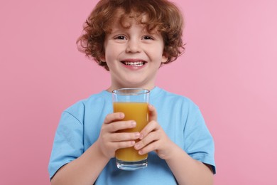 Photo of Cute little boy with glass of fresh juice on pink background