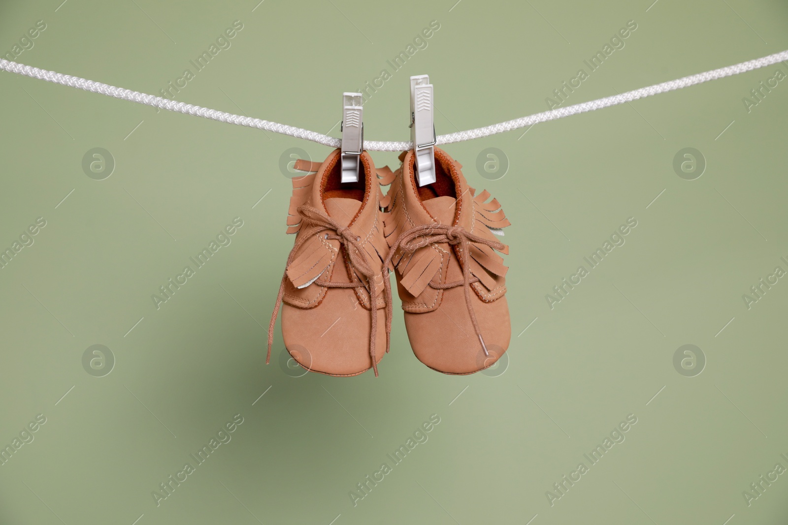 Photo of Cute small baby shoes hanging on washing line against green background