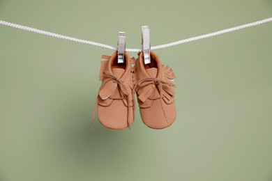 Cute small baby shoes hanging on washing line against green background