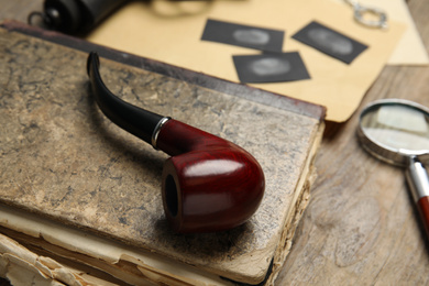 Photo of Tobacco pipe and old book on wooden table, closeup. Detective's workplace