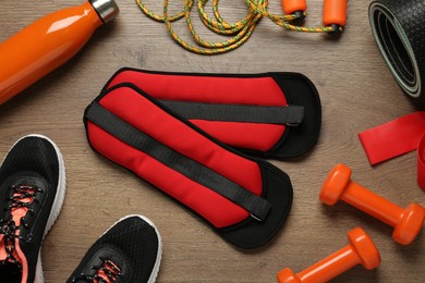 Red weighting agents and sport equipment on wooden table, flat lay